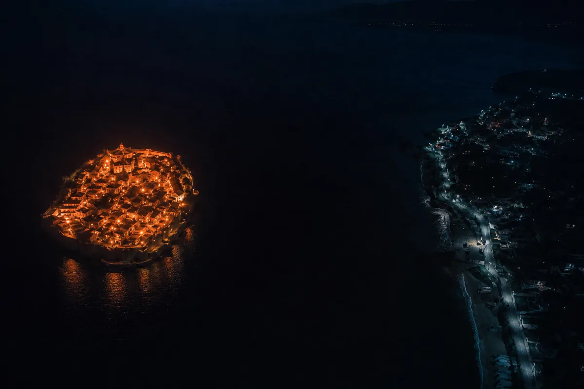 Isla iluminada y llena de vida separada de la costa apagada por un canal de agua negra sin ningún puente